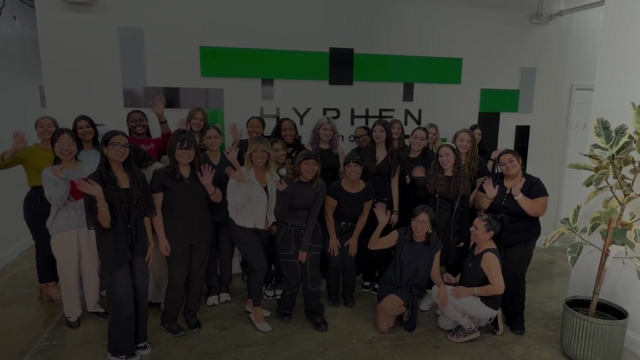 Hyphen Beauty + Massage School group photo in front of the Hyphen logo wall