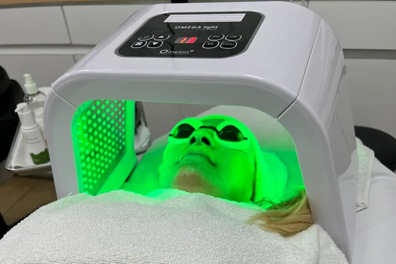 Client under an LED light therapy device during a facial at Hyphen Beauty + Massage School